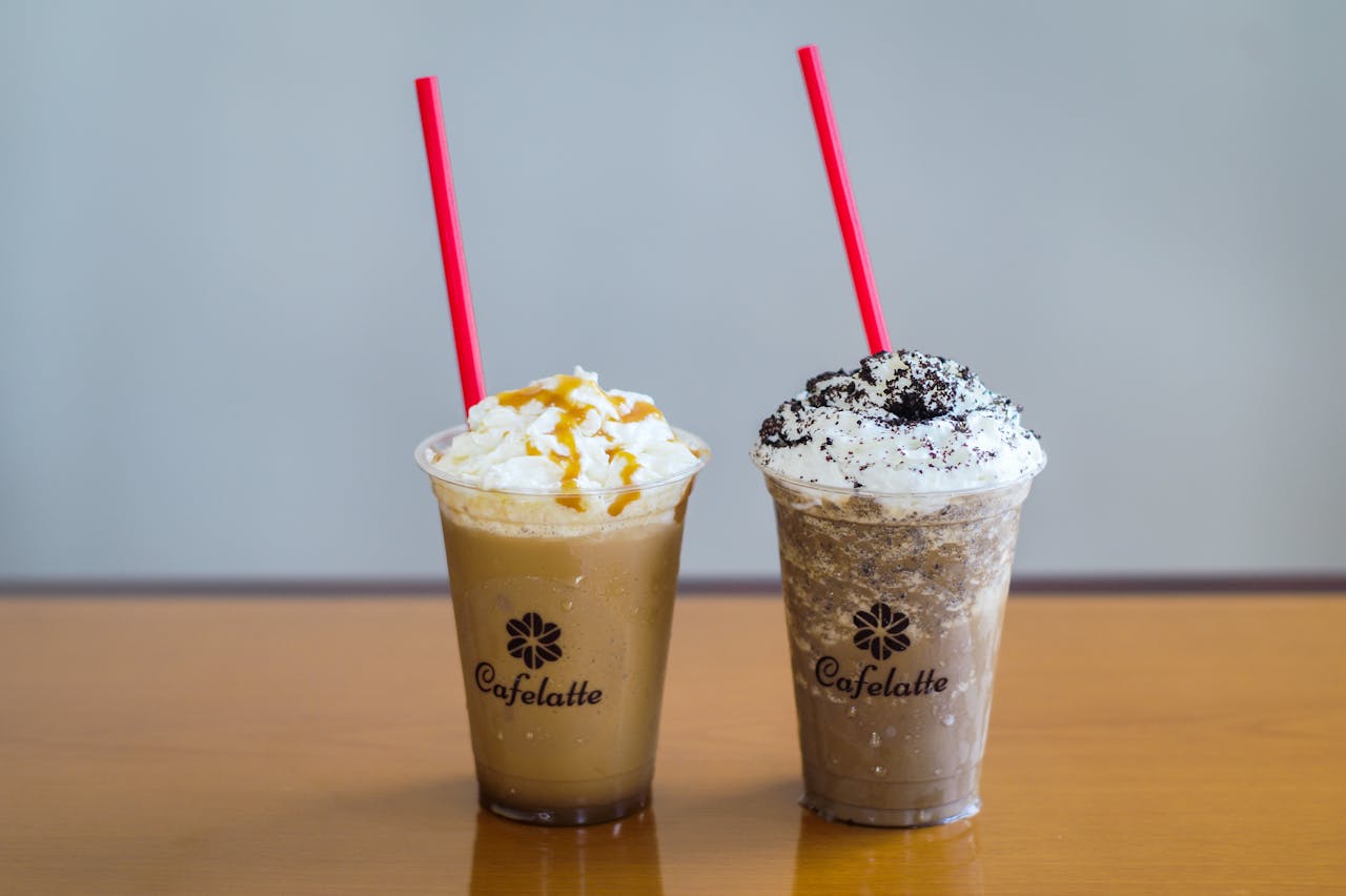 Crafting Captivating Headlines: Your awesome post title goes here Two cold coffee drinks with whipped cream and toppings, featuring red straws and branded cups on a wooden table.
