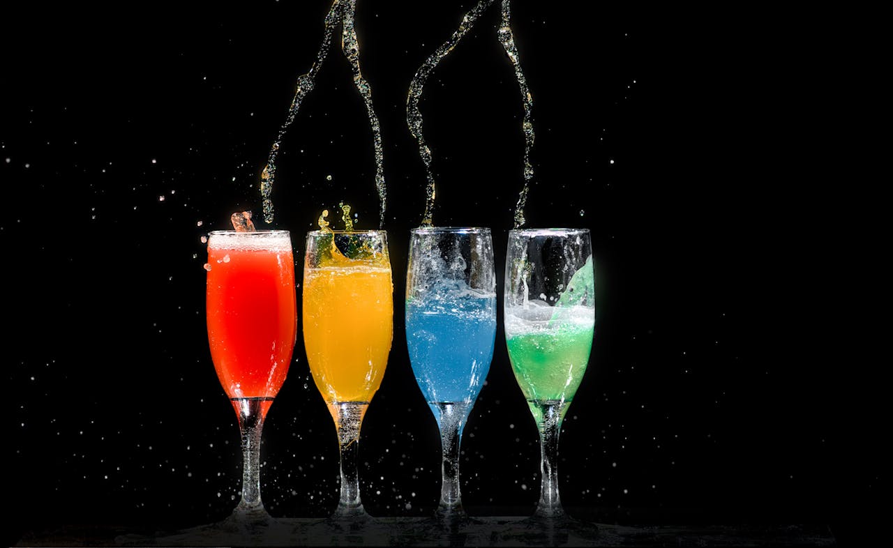 Home Vibrant colored cocktails splashing in glasses against a black background.