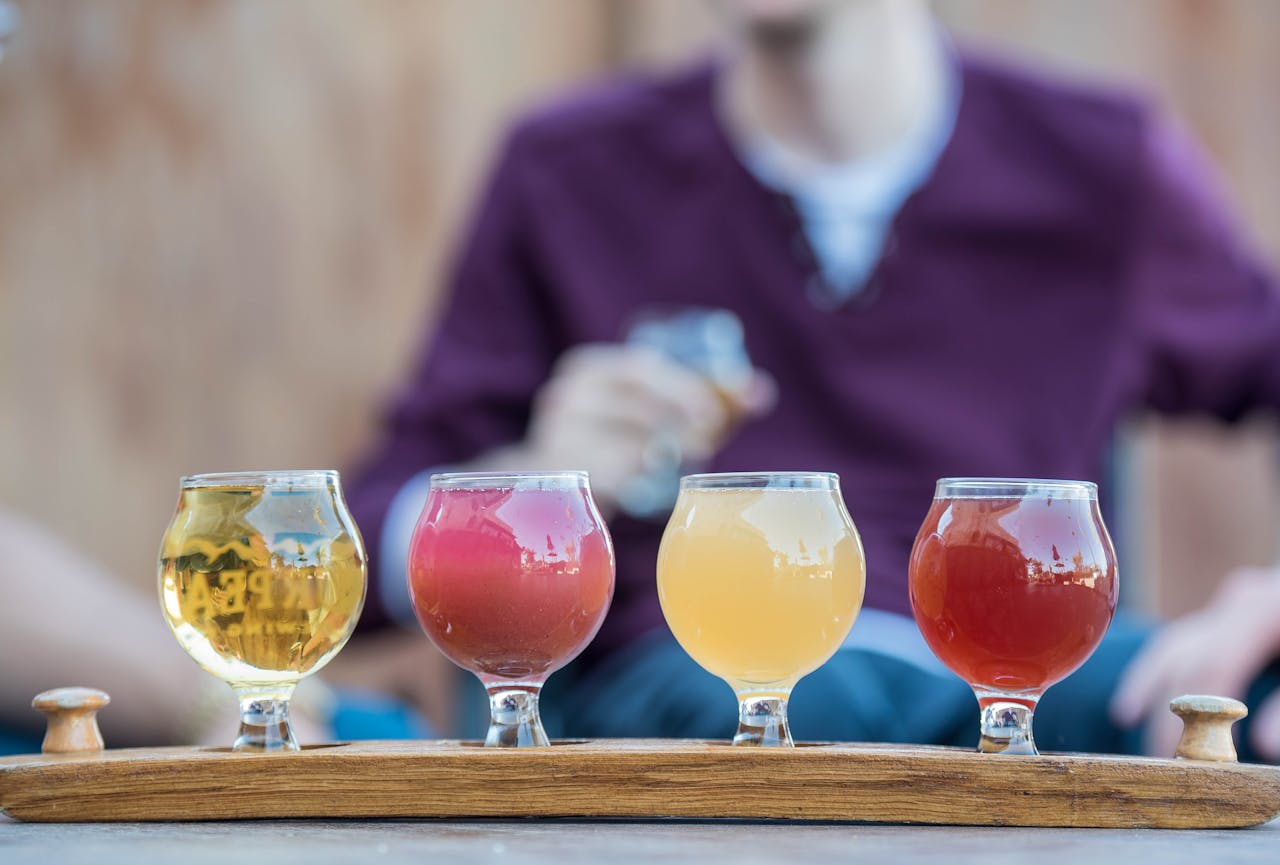 Home Selection of four craft beers in unique glasses on a wooden tray, with person in the background enjoying a drink.