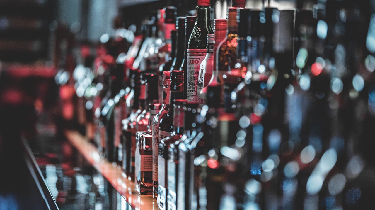 Home Blurred view of assorted alcohol bottles lined up on a bar shelf indoors.